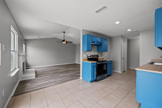 kitchen with blue cabinets, vaulted ceiling, light tile patterned floors, and stainless steel electric range