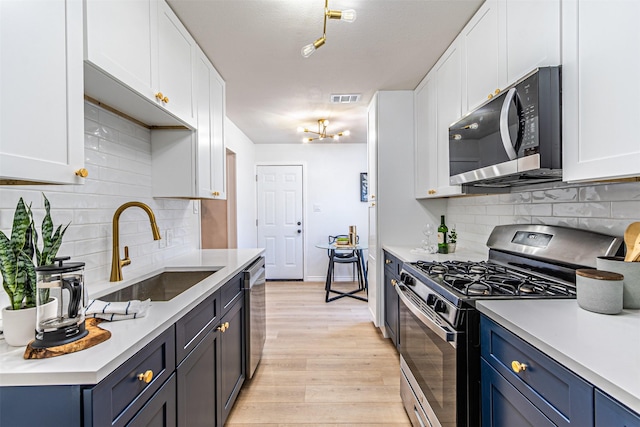 kitchen with sink, light hardwood / wood-style flooring, blue cabinetry, white cabinetry, and stainless steel appliances