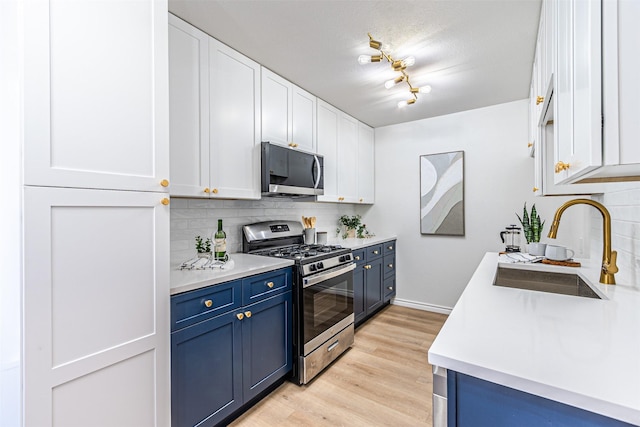 kitchen with blue cabinets, sink, stainless steel appliances, decorative backsplash, and white cabinets