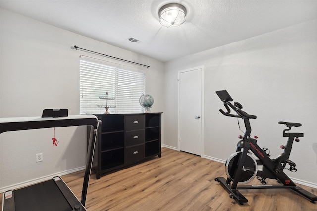 workout area with a textured ceiling and light wood-type flooring