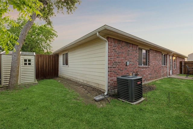 property exterior at dusk featuring a shed, cooling unit, and a lawn