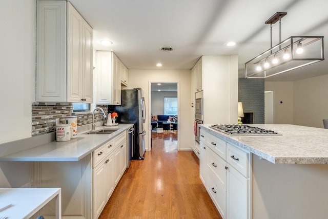 kitchen featuring sink, light hardwood / wood-style flooring, pendant lighting, stainless steel gas stovetop, and white cabinets