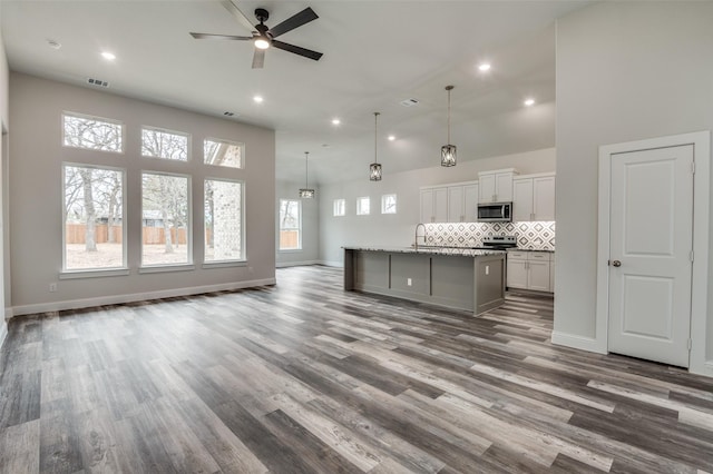 kitchen with white cabinetry, hanging light fixtures, light stone countertops, a center island with sink, and decorative backsplash