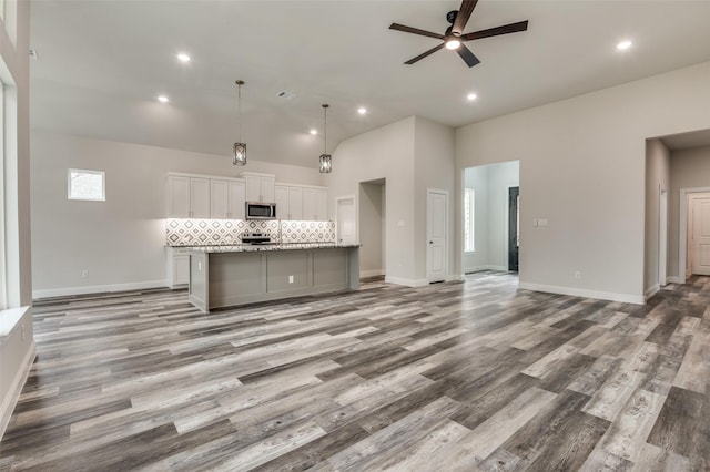 kitchen with appliances with stainless steel finishes, pendant lighting, tasteful backsplash, white cabinets, and a spacious island