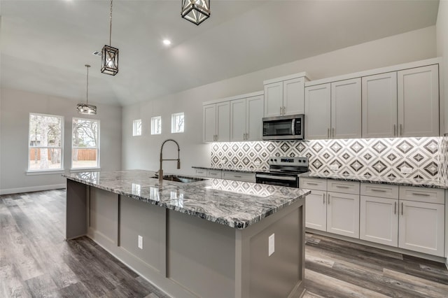 kitchen with sink, a center island with sink, pendant lighting, stainless steel appliances, and light stone countertops