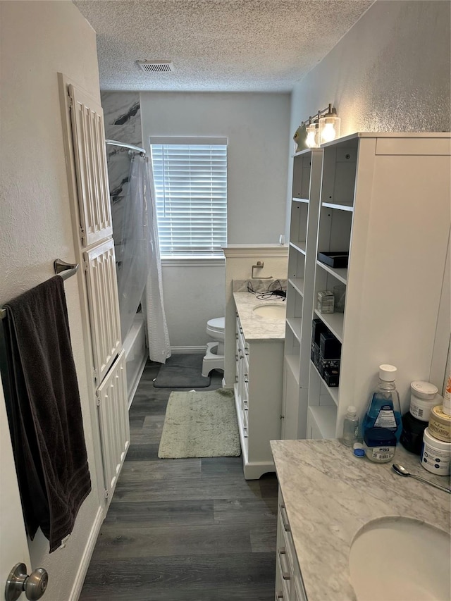 full bathroom with shower / bathtub combination with curtain, hardwood / wood-style flooring, vanity, a textured ceiling, and toilet