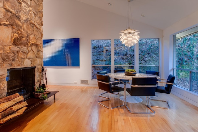 dining area featuring a healthy amount of sunlight, a stone fireplace, high vaulted ceiling, and light wood-type flooring