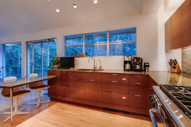 kitchen with sink, backsplash, stainless steel gas range, and light wood-type flooring