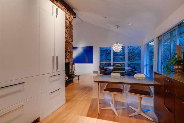 dining room featuring an inviting chandelier, a fireplace, high vaulted ceiling, and light hardwood / wood-style flooring