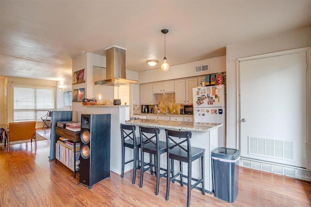 kitchen with hanging light fixtures, light hardwood / wood-style floors, island exhaust hood, kitchen peninsula, and white fridge