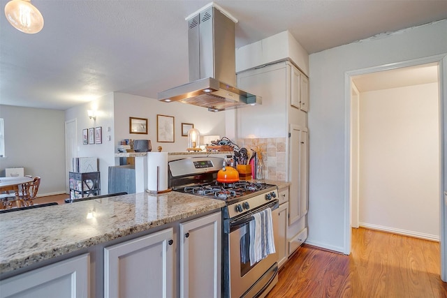 kitchen with island range hood, backsplash, light stone counters, stainless steel gas range, and light wood-type flooring