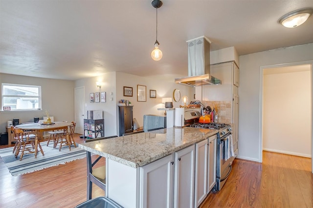 kitchen with decorative light fixtures, white cabinetry, island exhaust hood, light stone counters, and stainless steel gas range