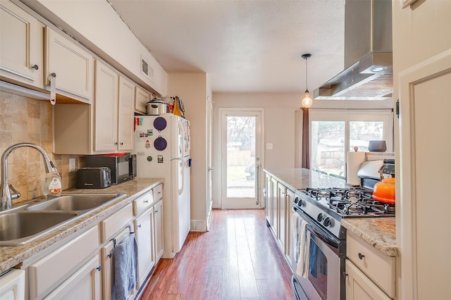 kitchen featuring pendant lighting, sink, stainless steel gas stove, white refrigerator, and exhaust hood