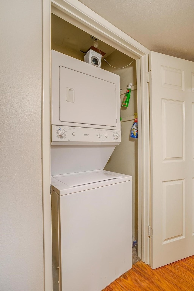 laundry area with stacked washer / dryer and light wood-type flooring