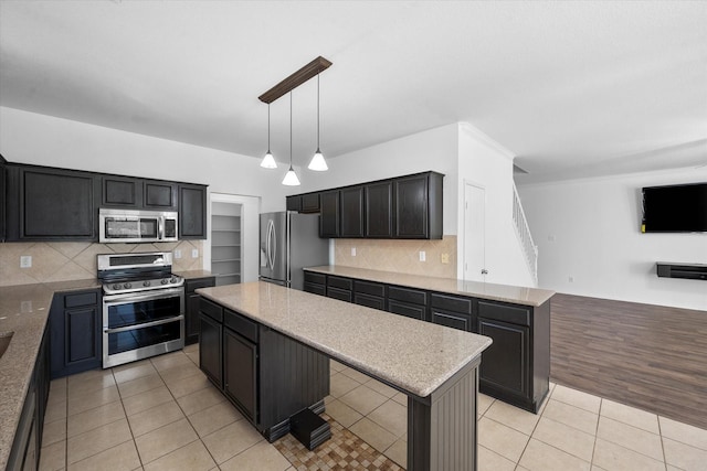 kitchen featuring light tile patterned floors, appliances with stainless steel finishes, a center island, decorative backsplash, and decorative light fixtures