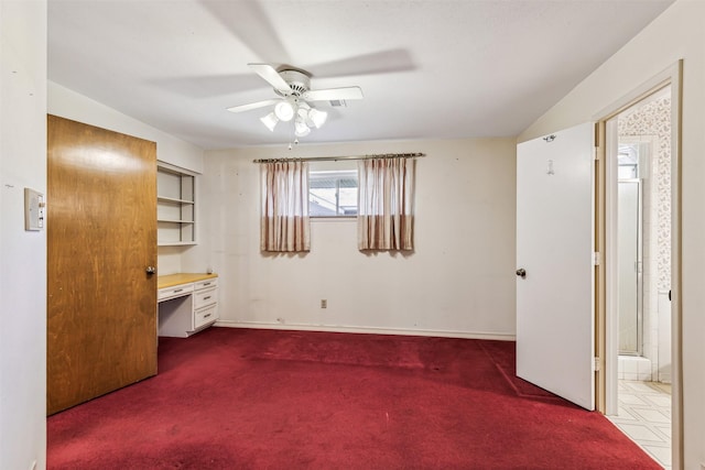 unfurnished bedroom featuring connected bathroom, built in desk, and dark carpet