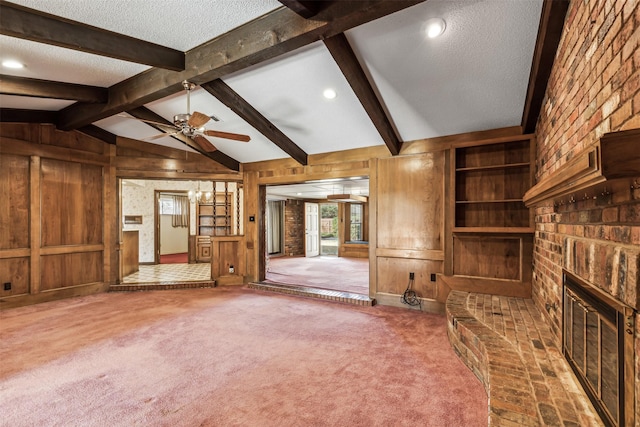 unfurnished living room featuring vaulted ceiling with beams, wooden walls, carpet floors, a fireplace, and a textured ceiling