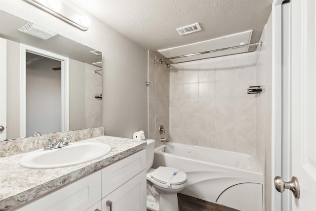 full bathroom featuring vanity, tiled shower / bath combo, toilet, and a textured ceiling