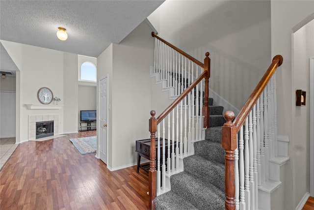 staircase featuring wood-type flooring, a tile fireplace, and a textured ceiling