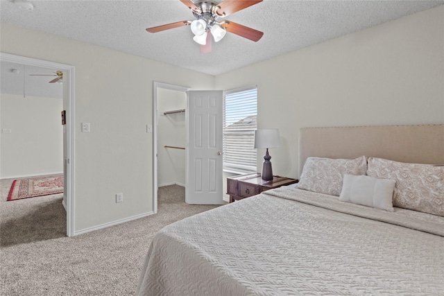 bedroom with ceiling fan, light colored carpet, a textured ceiling, and a walk in closet