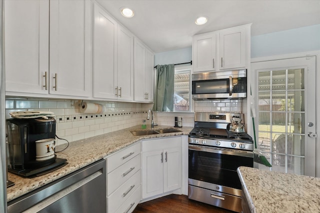 kitchen with appliances with stainless steel finishes, sink, white cabinets, decorative backsplash, and light stone countertops