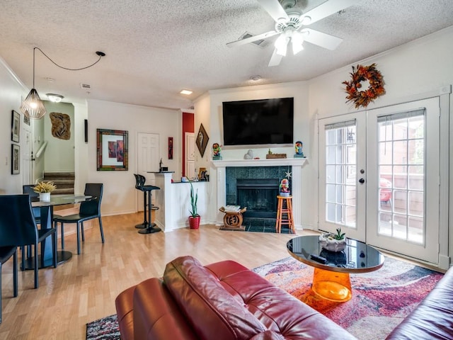 living room featuring a tile fireplace, wood-type flooring, ornamental molding, a textured ceiling, and french doors