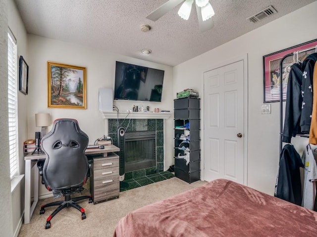 carpeted bedroom featuring a tiled fireplace, ceiling fan, and a textured ceiling