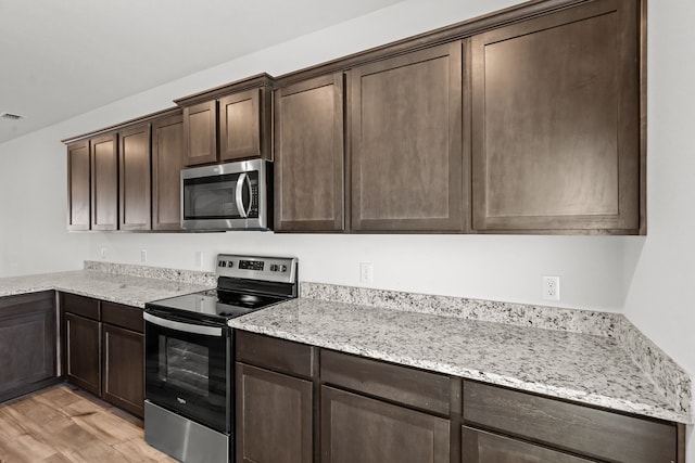 kitchen with appliances with stainless steel finishes, dark brown cabinets, light stone counters, and light hardwood / wood-style floors