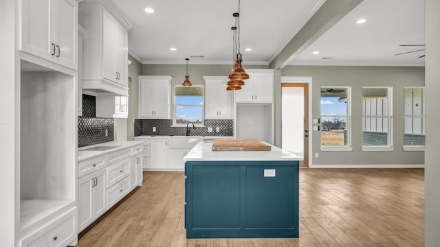 kitchen with white cabinetry, decorative light fixtures, ornamental molding, a kitchen island, and light hardwood / wood-style floors