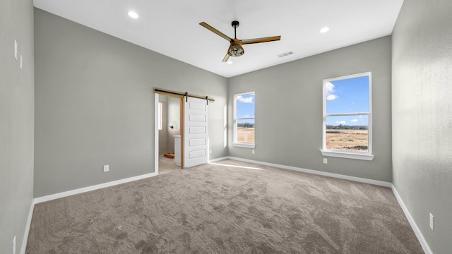 unfurnished bedroom with light carpet, multiple windows, a barn door, and ceiling fan