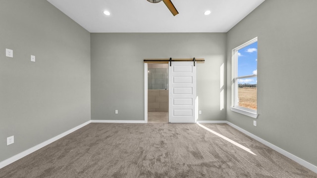 unfurnished bedroom featuring a barn door, carpet, ceiling fan, and ensuite bath