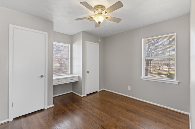 unfurnished bedroom featuring built in desk, dark hardwood / wood-style floors, and ceiling fan