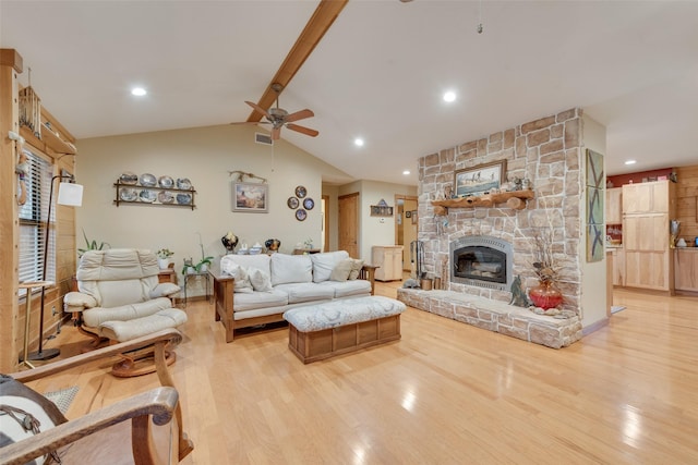 living room with ceiling fan, a stone fireplace, lofted ceiling with beams, and light hardwood / wood-style flooring