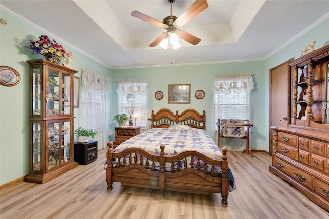 bedroom with a tray ceiling, ornamental molding, light hardwood / wood-style floors, and a textured ceiling