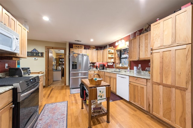 kitchen with appliances with stainless steel finishes, sink, light stone counters, and light hardwood / wood-style flooring