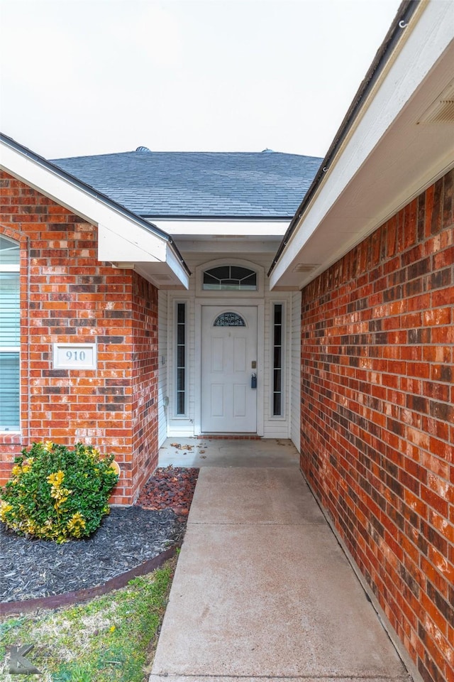 property entrance featuring brick siding and roof with shingles