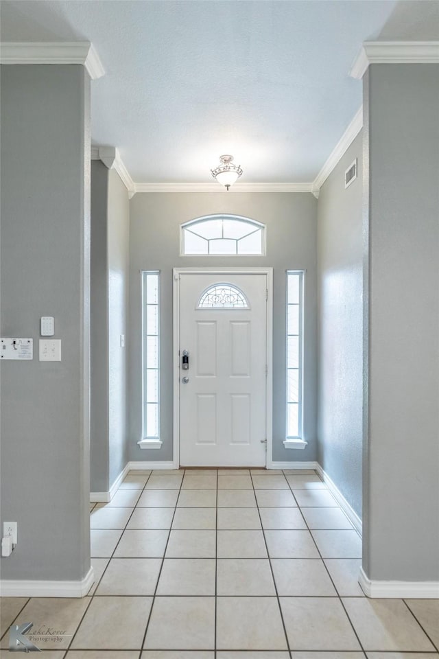 entryway with light tile patterned floors, baseboards, visible vents, and crown molding