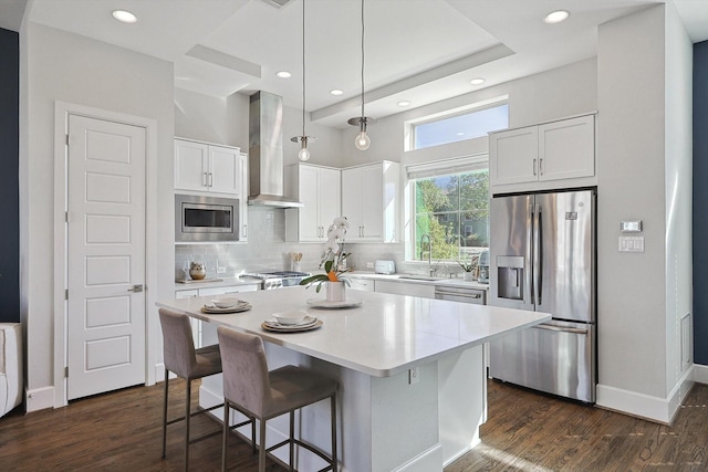 kitchen with wall chimney exhaust hood, white cabinetry, a kitchen island, pendant lighting, and stainless steel appliances