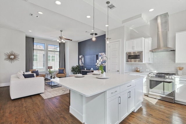 kitchen with pendant lighting, white cabinetry, stainless steel appliances, a kitchen island, and wall chimney exhaust hood