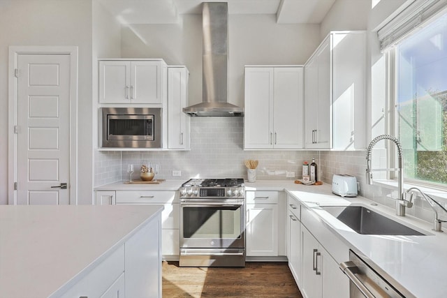 kitchen featuring white cabinets, stainless steel appliances, decorative backsplash, and wall chimney range hood