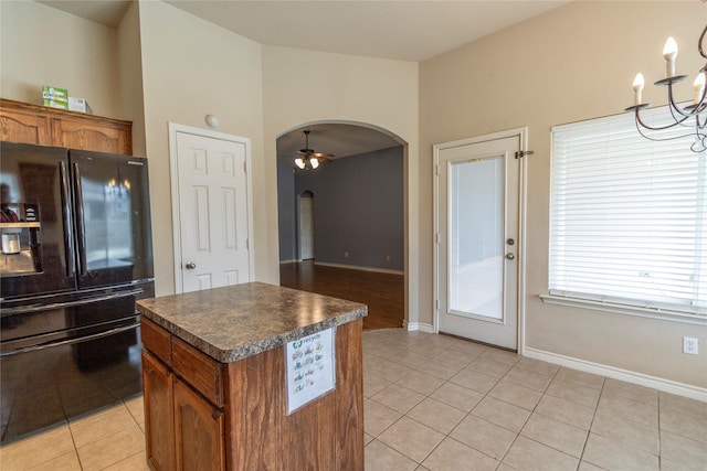 kitchen with light tile patterned flooring, a kitchen island, ceiling fan with notable chandelier, and black refrigerator with ice dispenser