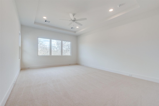 empty room with ceiling fan, a tray ceiling, and light carpet