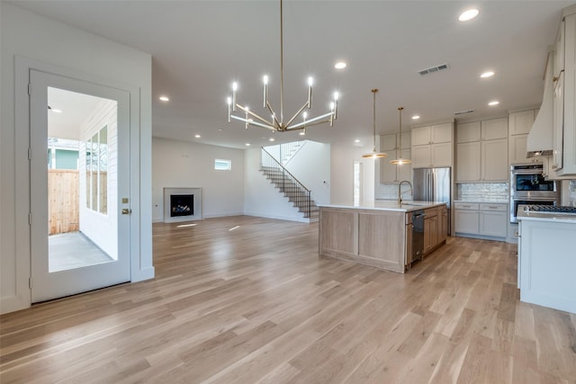 kitchen with decorative light fixtures, a large island with sink, stainless steel appliances, light hardwood / wood-style floors, and decorative backsplash