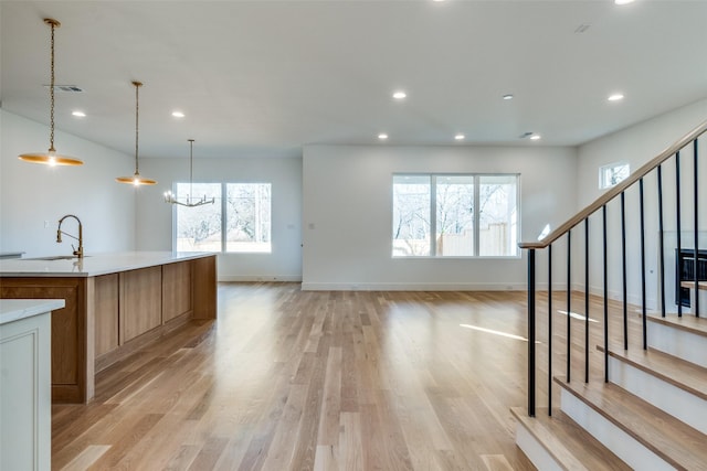 kitchen with pendant lighting, sink, light wood-type flooring, a large island with sink, and an inviting chandelier