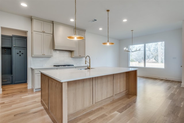 kitchen with a kitchen island with sink, sink, hanging light fixtures, and premium range hood