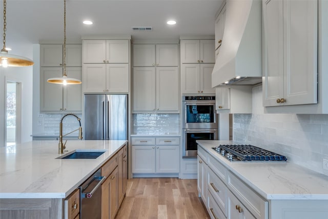 kitchen featuring sink, white cabinetry, custom range hood, pendant lighting, and stainless steel appliances