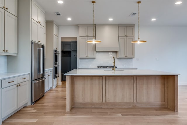 kitchen with pendant lighting, light hardwood / wood-style flooring, premium range hood, stainless steel appliances, and a center island with sink