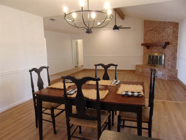 dining area with vaulted ceiling with beams, a fireplace, and light hardwood / wood-style floors