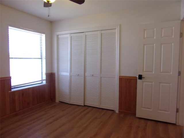 unfurnished bedroom with ceiling fan, wooden walls, dark hardwood / wood-style flooring, and a closet