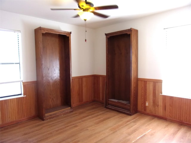 empty room with light hardwood / wood-style floors, ceiling fan, and wood walls